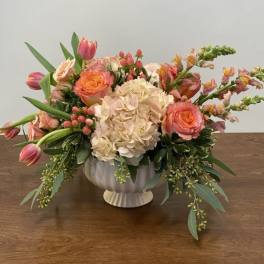 Peach and pink floral arrangement in a white pedestal vase