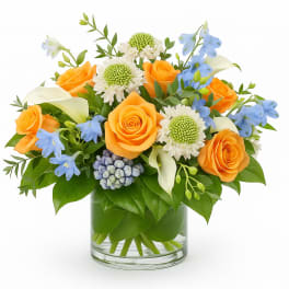 Orange roses with blue flowers and white calla lilies in a glass vase