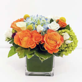 Orange roses and mixed blooms in a square glass vase