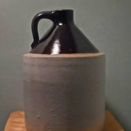 Dark ceramic jug in a beige sleeve on a wooden surface