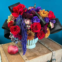 Bouquet of red roses, purple blooms, and orange chrysanthemums in a pale vase