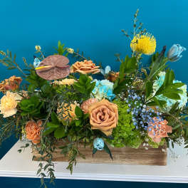 Mixed floral arrangement in a wooden box with peach roses and blue hydrangeas