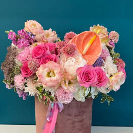 Pink and peach floral arrangement in a velvet hatbox with ribbon