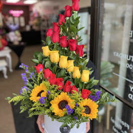 Tiered arrangement of red and yellow roses with sunflowers in a white box
