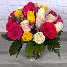 Mixed roses in a clear glass vase with small purple filler flowers