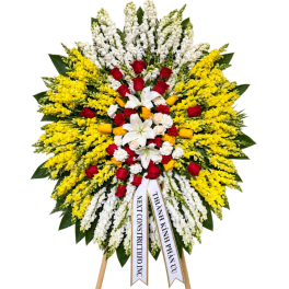Large standing floral wreath with red, white, and yellow flowers on ribbons