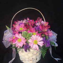 Pink and purple daisy basket arrangement with sheer ribbon bows in a white woven basket