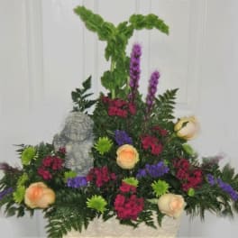 Mixed floral arrangement with peach roses, purple blooms, and a small angel statue