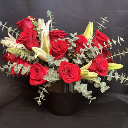 Red roses and white lilies in a black vase with trailing eucalyptus