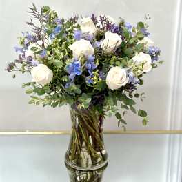 White roses and blue flowers in a clear glass vase