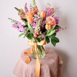 Orange and pink mixed bouquet in a clear glass vase with ribbon