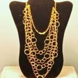 Layered gold-toned necklace displayed on a black bust stand