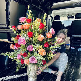 Large mixed rose arrangement in a silver vase with a woman beside it