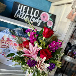 Bouquet of red roses, pink lilies, and purple flowers in a white mug vase