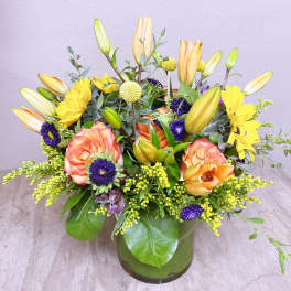 Mixed bouquet of lilies, roses, and yellow daisies in a glass vase