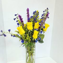 Yellow roses and blue-purple flowers in a clear glass vase