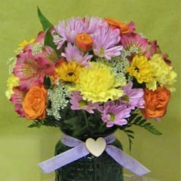 Mixed bouquet of pink, yellow, and orange flowers in a dark vase with a ribbon