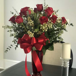 Red roses in a tall vase with a large red ribbon