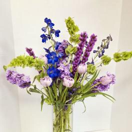 Tall vase arrangement with blue, purple, and pale pink flowers