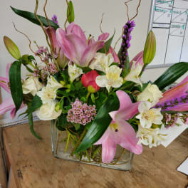 Pink lilies and white flowers arranged in a clear glass vase