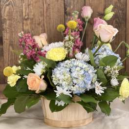 Mixed bouquet in a wooden basket with roses, hydrangea, and daisies