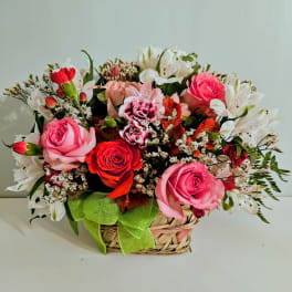 Mixed pink and red flower arrangement in a woven basket with a green ribbon
