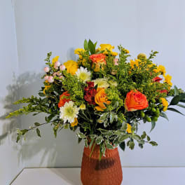 Mixed bouquet of orange, yellow, and white flowers in a textured vase