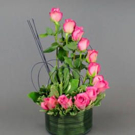 Pink roses arranged in a green round vase with decorative wire accents