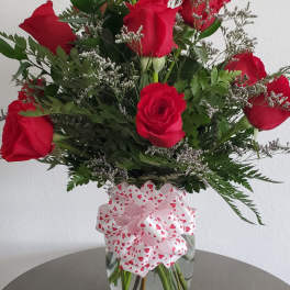 Red roses arranged in a clear glass vase with a heart-patterned bow