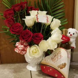 Red and white roses in a white vase with chocolates and a teddy bear