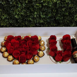 Red roses arranged with chocolates and a Baileys bottle in a gift box