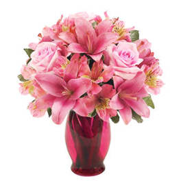 Pink lilies and roses arranged in a pink glass vase.
