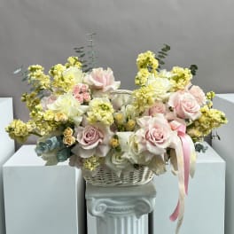 Basket arrangement of pale pink and white roses with yellow blooms and ribbon