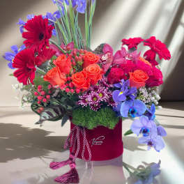 Mixed bouquet with orange roses, red gerberas, and purple orchids in a red hat box