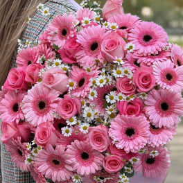 Pink gerbera daisies and roses in a hand-held bouquet