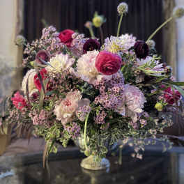 Large mixed floral arrangement in a pedestal vase with pink, white, and purple blooms