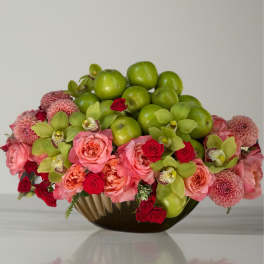 Pink and red floral arrangement with green apples in a low vase