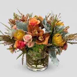 Mixed bouquet of orange, pink, and yellow flowers in a clear glass vase
