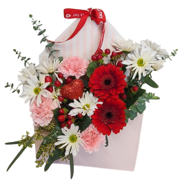 Envelope-shaped pink box filled with red gerbera daisies, white daisies, pink carnations, and a red glitter heart pick.