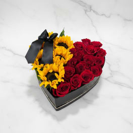 Heart-shaped box with red roses and yellow sunflowers tied with a black ribbon