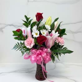 Bouquet of red roses, pink lilies, and white daisies in a vase with a pink bow