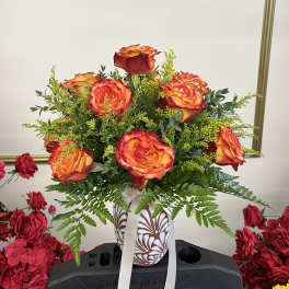 Orange-red roses in a patterned vase with a white ribbon