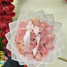 Pink rose bouquet wrapped in sheer paper with a satin ribbon and pearl accents