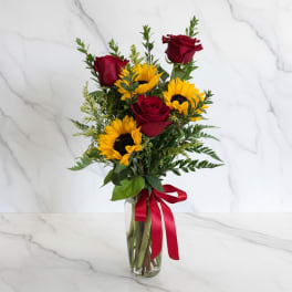 Red roses and yellow sunflowers in a glass vase with a red ribbon