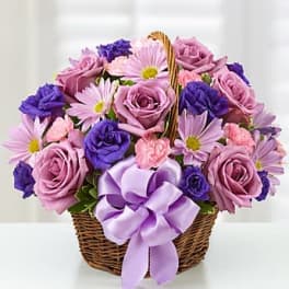 Basket of lavender roses, pink daisies and carnations, and purple blooms with a large lavender bow