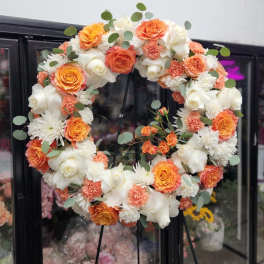 Round floral wreath of orange, white, and peach blooms on a stand