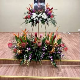 Large tropical floral tribute with white and purple flowers on a stand