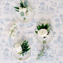 Small white floral boutonnieres on plates with dark green leaves