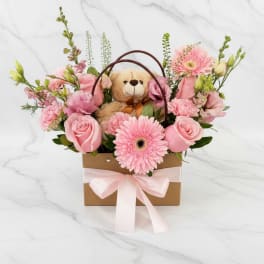 Pink flower basket with a teddy bear and ribbon