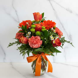 Orange and coral bouquet in a glass vase with a ribbon